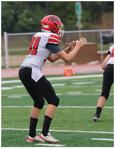A person wearing a white and red football jersey with the number 21 and black pants is in a crouched position on a football field. Description generated by AI