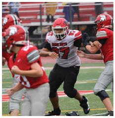 A person wearing a red and white football uniform with the number 87 is running on a field while two other players in red uniforms attempt to block or tackle. Description generated by AI