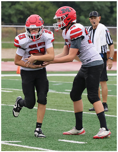 A person wearing a white and red football uniform is running on a field while holding a football and being assisted by another person. Description generated by AI