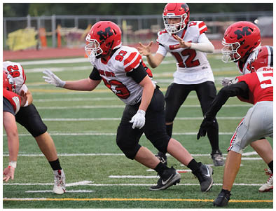 People in football uniforms are actively engaged in a play on a green field with white yard lines. Description generated by AI