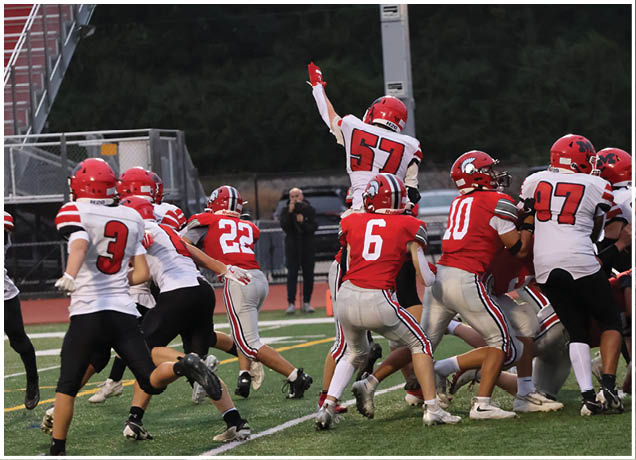 Three people in football uniforms are actively playing on a field, with one person holding a football and another running toward them. Description generated by AI