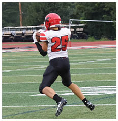 A person wearing a sports uniform with the number 25 is running on a green football field. Description generated by AI