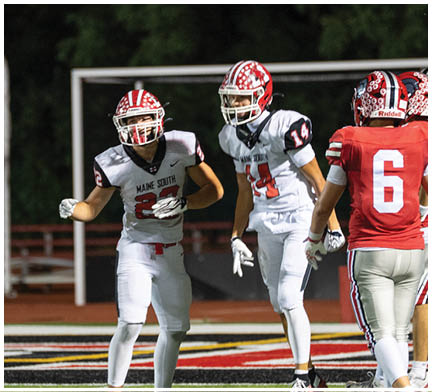 Several people wearing football uniforms are standing on a field near a goalpost, with some facing each other and others looking away. Description generated by AI