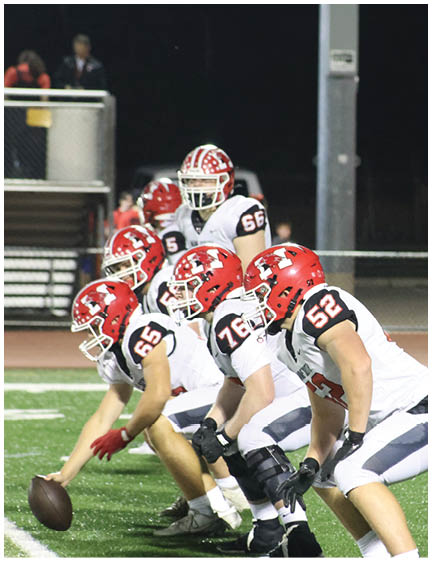 A person wearing a red helmet and white football uniform is running on a green football field while holding a football. Description generated by AI