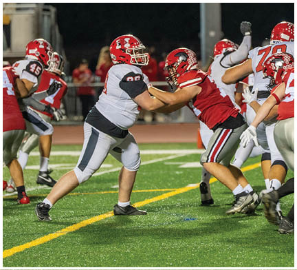 People wearing football uniforms are actively engaged in a game on a well-lit field at night. Description generated by AI