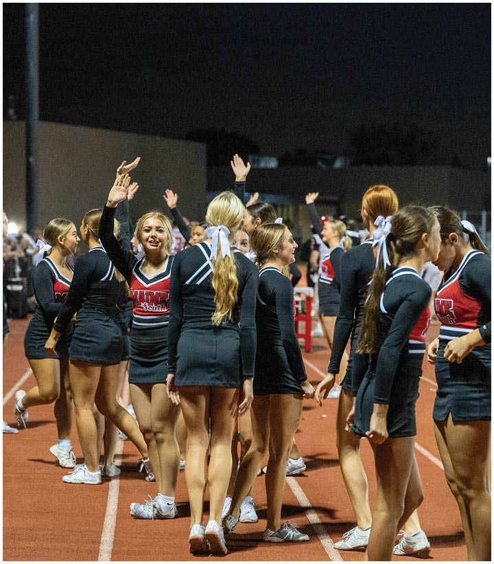 A group of adults in cheerleading uniforms are standing and interacting on a track at night. Description generated by AI
