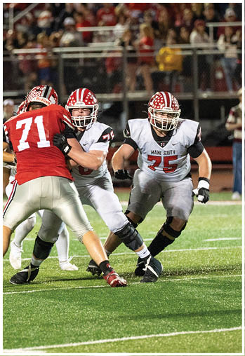 Two people in white football uniforms are blocking a person in a red football uniform during a game on a field with a crowd in the background. Description generated by AI