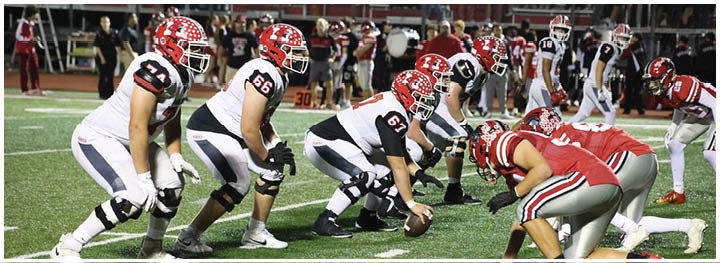 Two opposing American football teams are lined up facing each other on a field, ready for the next play. Description generated by AI