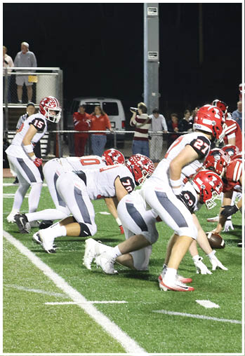 Two opposing American football teams are lined up at the line of scrimmage on a well-lit field during a nighttime game. Description generated by AI