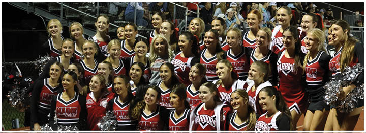 A large group of people dressed in red and black cheerleading uniforms are posing together and smiling in a stadium setting. Description generated by AI