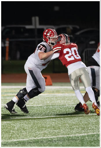 Several people wearing football uniforms are engaged in a play on a well-lit field at night. Description generated by AI