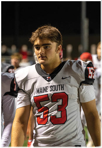 A person wearing a white football jersey with the number 53 and the words Maine South stands on a field at night. Description generated by AI