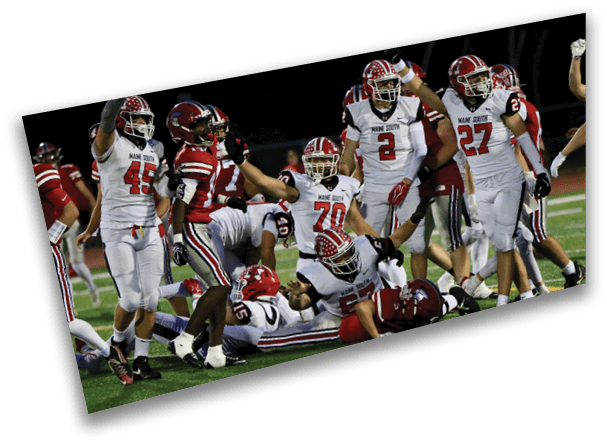 A group of football players in white and red uniforms are gathered on a field with one player on the ground being tackled by players in red uniforms. Description generated by AI