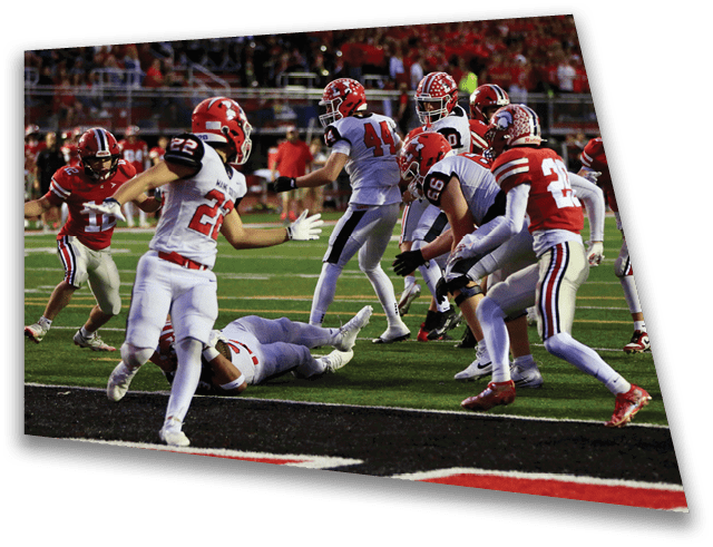 Several people wearing football uniforms are actively engaged in a play on a football field during a game. Description generated by AI