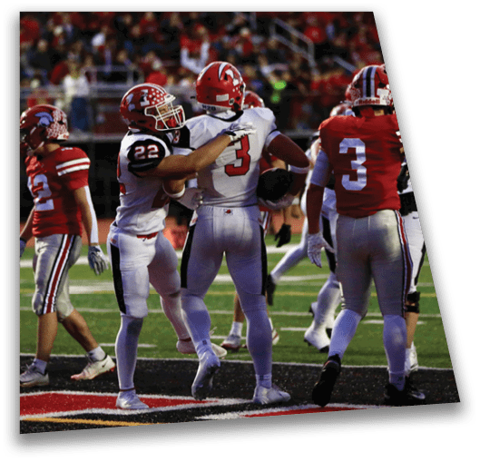 Two people in football uniforms are celebrating on a field, with one holding a football and the other placing a hand on their shoulder. Description generated by AI