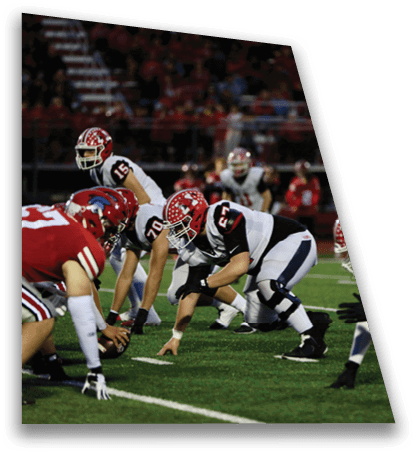 Two football players in white and black uniforms with red helmets are crouched in a ready position on a green field during a game. Description generated by AI
