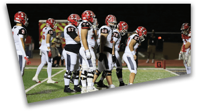 A group of football players in red helmets and white uniforms are lined up on a field preparing for a play. Description generated by AI
