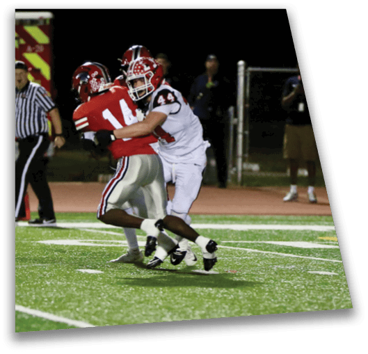 Two people in football uniforms are engaged in a tackle on a grassy field during a nighttime game. Description generated by AI
