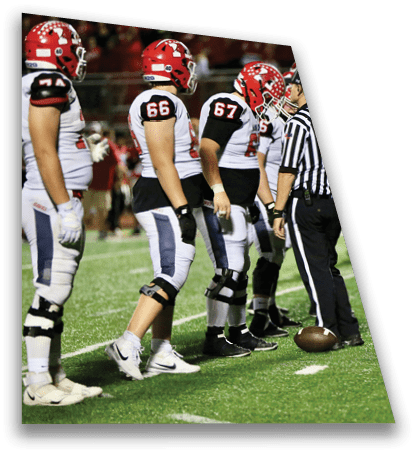 A referee stands on a football field with a football at their feet while several players in red and white uniforms stand nearby. Description generated by AI