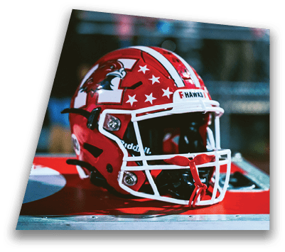 A red and white football helmet with star decals and the word “HAWKS" on the front is resting on a red surface. Description generated by AI