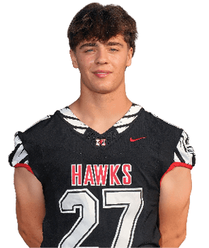 A person with short curly hair is standing with hands behind their back wearing a black sports jersey with the word “HAWKS" and the number 27 on the front. Description generated by AI