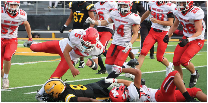 Two people in football uniforms are lying on the grass field, one wearing a yellow helmet and black uniform and the other wearing a red helmet and red and white uniform. Description generated by AI