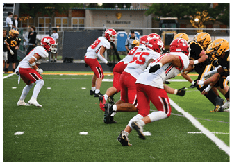 Two opposing football teams in red and white and black and yellow uniforms are lined up facing each other on a green field during a game. Description generated by AI