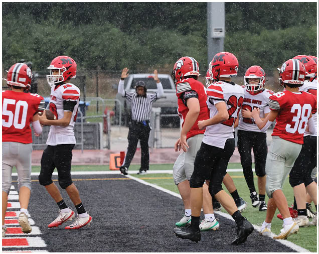 Several people wearing red and white football uniforms are on a field with a referee raising both hands in the background. Description generated by AI