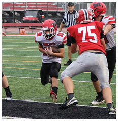 A group of people wearing football uniforms are actively engaged in a play on a football field with a referee observing in the background. Description generated by AI
