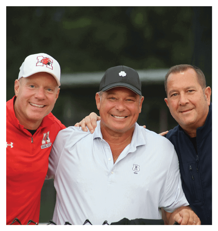Three adults smiling and standing close together outdoors, with one wearing a white cap and red jacket, another in a white polo shirt and black cap, and the third in a dark jacket. Description generated by AI