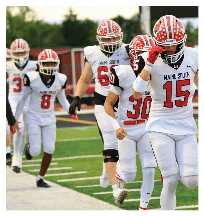 Four people in white football uniforms with red helmets and red numbers are walking on a football field. Description generated by AI
