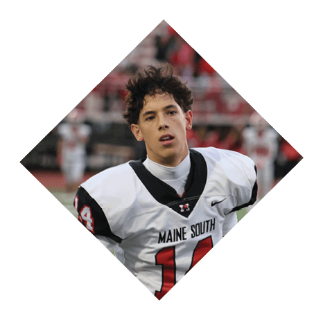 A person wearing a white and black sports jersey is on a field with blurred figures and red seating in the background. Description generated by AI