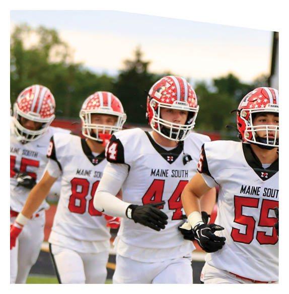 Adults in white football uniforms with red helmets and black gloves are running together on a green field. Description generated by AI