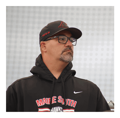 A person wearing glasses and a black Nike hoodie with red and white text is looking to the side against a blurred background. Description generated by AI