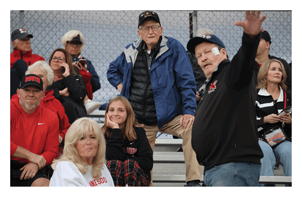 A group of people sitting and standing on bleachers with one person resting their chin on their hand and smiling. Description generated by AI