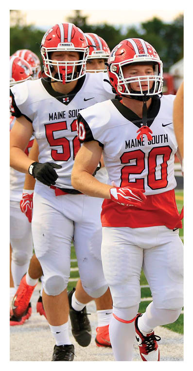 A group of people wearing red helmets and white football uniforms with red and black details are walking in a line outdoors. Description generated by AI