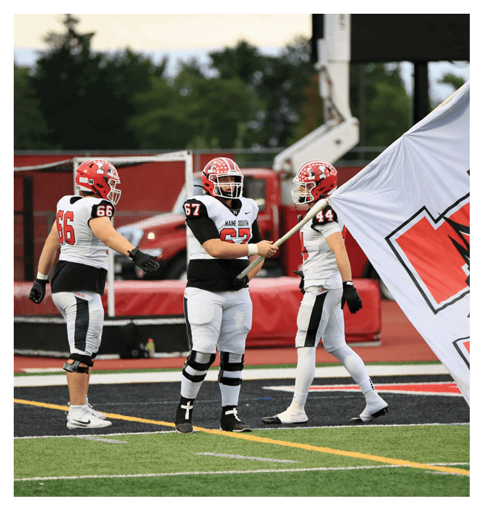 Three people wearing football uniforms and helmets stand on a field with one holding a flag. Description generated by AI