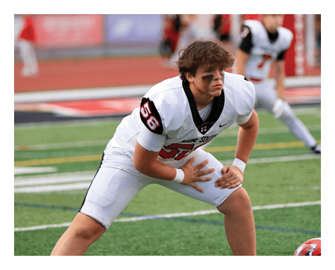 A person in a white football uniform with black and red accents is crouched on a green field, appearing focused and ready for action. Description generated by AI