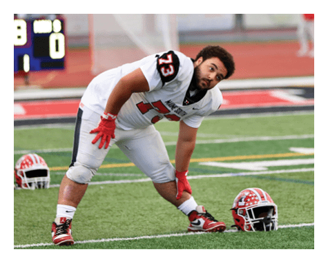 A person in a white football uniform with the number 73 is bending forward on a football field near a red and white helmet placed on the ground. Description generated by AI