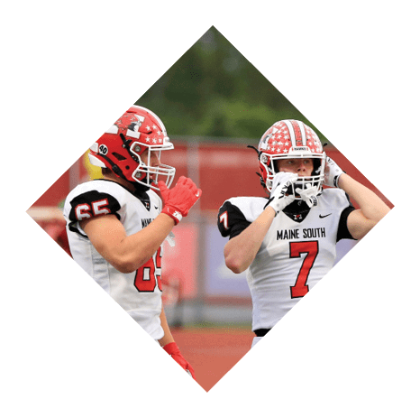 Two people wearing football uniforms and helmets stand on a field with one adjusting their helmet and the other holding their hand near their mouth. Description generated by AI