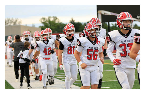 People wearing white and red football uniforms with helmets are walking on a field during a game or practice. Description generated by AI