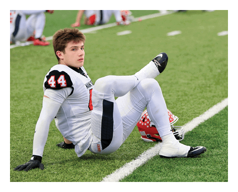 A person in a white football uniform with the number 44 is sitting on the grass field next to a red helmet. Description generated by AI