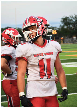 A person wearing a red and white football uniform with the words Maine South and the number 11 on the jersey stands on a football field with two other similarly dressed people in the background. Description generated by AI