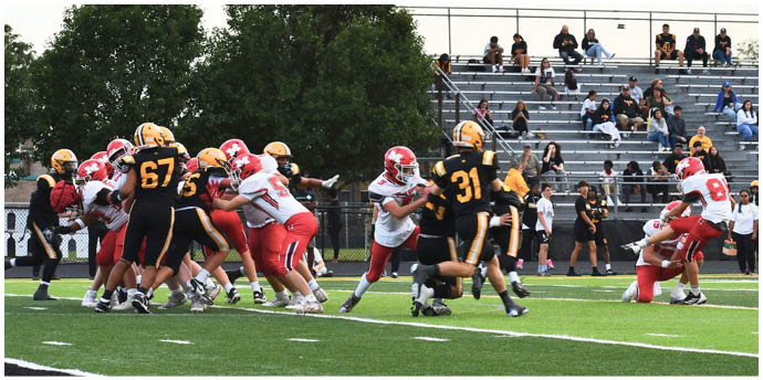 Players in black and yellow and white and red uniforms are engaged in a football game on a field with spectators watching from bleachers in the background. Description generated by AI