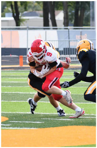 A group of people wearing football uniforms are playing on a field with one person in red and white being tackled by two people in black and yellow. Description generated by AI