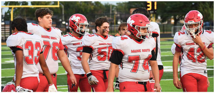 A group of people wearing red and white football uniforms are standing on a field with a scoreboard and goalpost visible in the background. Description generated by AI