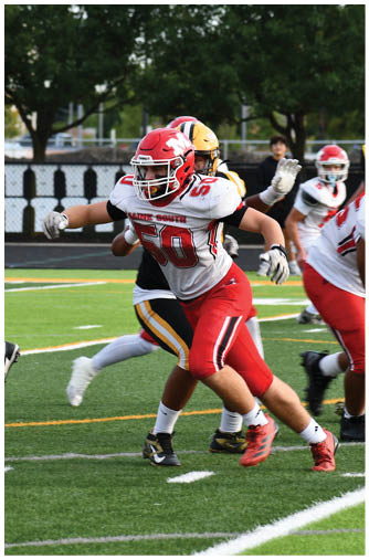 Players in red and white uniforms and players in black and yellow uniforms are engaged in a football game on a green field with white yard lines. Description generated by AI