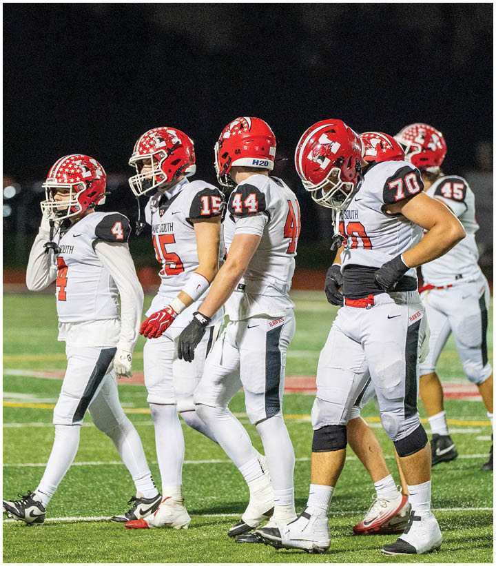 Two people wearing white football uniforms with red helmets and numbers stand on a field at night. Description generated by AI