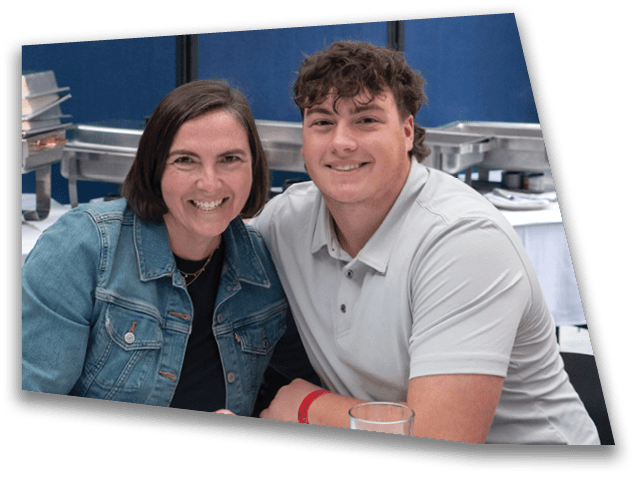 Two people smiling and sitting closely together at a table in a casual indoor setting with food trays in the background. Description generated by AI