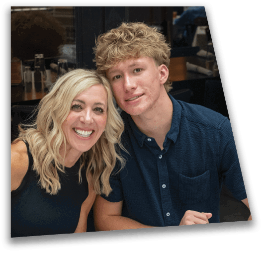 Two adults with light-colored hair are sitting closely together indoors, smiling at the camera, with one wearing a dark sleeveless top and the other a dark short-sleeve button-up shirt. Description generated by AI